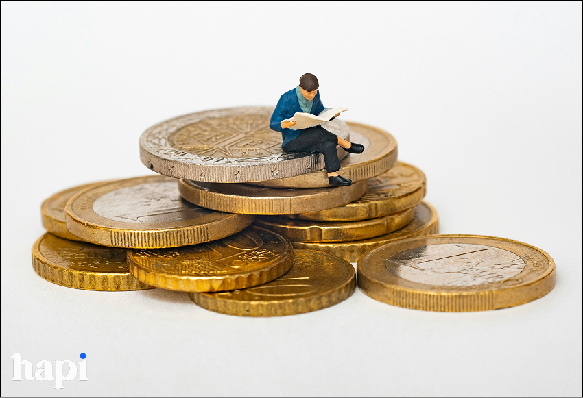 picture of coins with a tiny man sitting on them and reading a newspaper