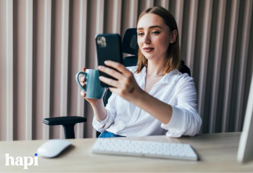 A woman looking pensively at a phone sitting at a desk