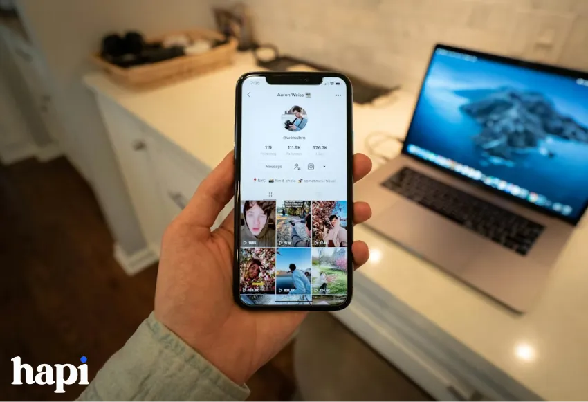a hand holding a phone, the screen shows a TikTok profile page
