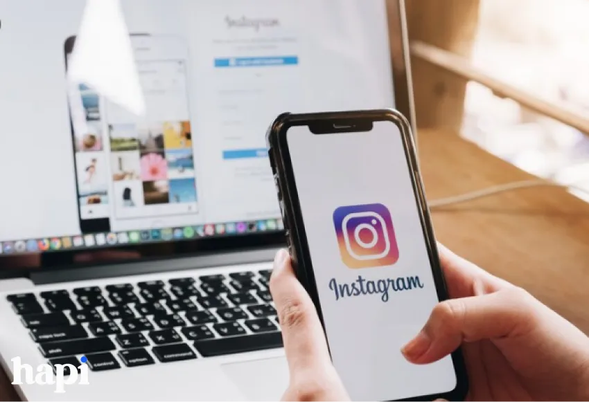someone holding a phone with Instagram logo on it and a laptop behind it with Instagram opened