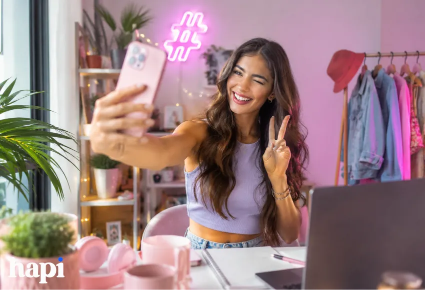 A woman in a room taking a selfie with a hashtag symbol above her head