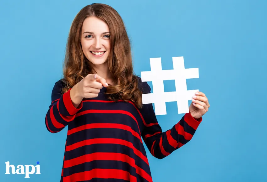 A woman holding a Hashtag symbol and pointing to the viewer
